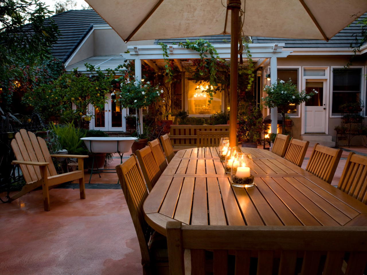 Outdoor dining area with a wooden table and chairs, surrounded by greenery and candles.