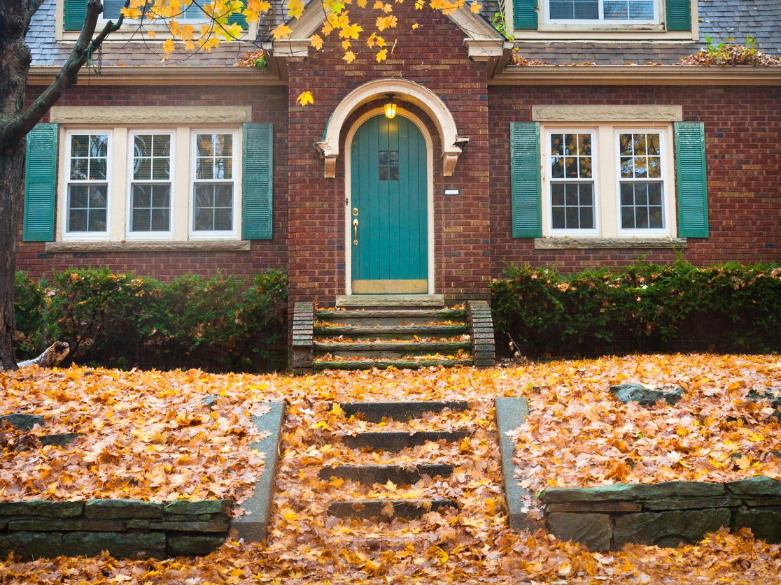 A brick house with a teal door surrounded by autumn leaves.